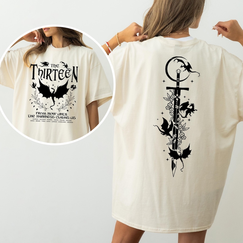May include: A white t-shirt with a black graphic on the front that says "The Thirteen" and a black graphic on the back featuring a sword with dragons and stars. The text on the front reads "From now until the darkness claims us."