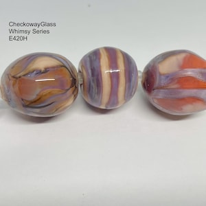 May include: Three glass beads with a swirl pattern in shades of purple, orange, and brown. The beads are strung on a wire with a silver loop at one end. The beads are part of the CheckowayGlass Whimsy Series E420H.