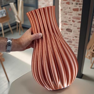 Può includere: Un vaso color rame con un design strutturato e a coste. Il vaso ha una base bulbosa e una parte superiore svasata. La superficie presenta delle scanalature verticali, creando un motivo visivamente interessante. Il vaso è esposto su una superficie di colore neutro.