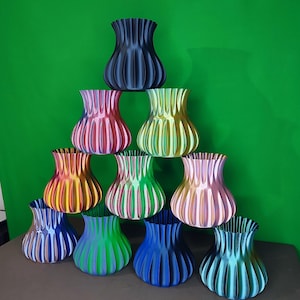 Peut inclure: Une collection de dix vases décoratifs de différentes couleurs, disposés en pyramide. Les vases ont un design côtelé et une forme arrondie. Les couleurs incluent le bleu, le rose, le vert, le jaune et l'orange. Le fond est vert uni.