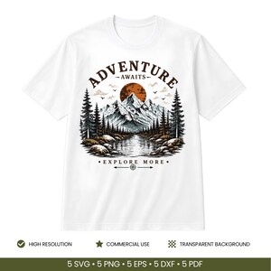 May include: A white t-shirt featuring a graphic illustration of a mountain range, a forest, and a lake under a dark orange sun. The text ADVENTURE AWAITS is arched above the mountains, and EXPLORE MORE is printed below the lake with a compass icon.