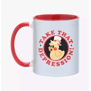 Puede incluir: Taza de cerámica blanca con interior y asa rojos. La taza presenta un pato de dibujos animados con sombrero de copa, rodeado por el texto "TAKE THAT DEPRESSION!" en un diseño circular. El pato tiene mejillas rosadas.