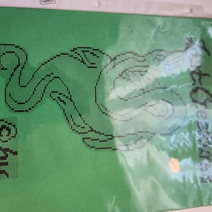 May include: Green cross-stitch pattern with a black and white design of a mermaid with the text "Little Green Mermaids" on the right side of the image.