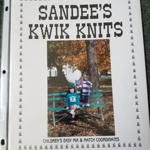 May include: A book cover for a knitting pattern book titled "Sandee's Kwik Knits". The cover features a photo of two children sitting on a bench in a park. The children are holding balloons and wearing colorful clothing. The book is titled "Children's Easy Mix & Match Coordinates" and is by Sandee Cherry. The book number is 13.