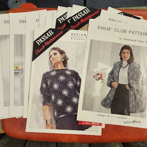 May include: A stack of vintage knitting pattern booklets with a red, white, and black color scheme. The patterns are for a black and white sweater with a geometric design and a black and white jacket with a checkered pattern. The text on the cover reads "PASSAP Club Pattern" and "Design No 11 'Checkers' by Eileen Metcalf".
