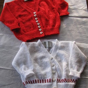 Pode incluir: Dois cardigãs de malha, um vermelho com botões de coração branco e outro branco com listras vermelhas e botões brancos.
