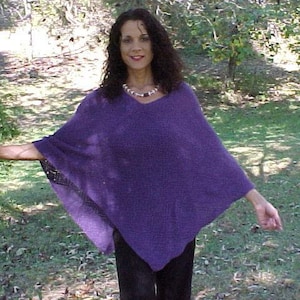 May include: A woman wearing a purple knitted poncho with a beaded necklace. The poncho has a loose fit and a long, flowing design.