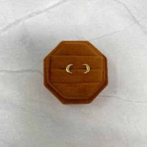 May include: A pair of gold crescent moon earrings in a brown velvet jewellery box.