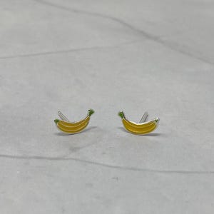 May include: A pair of silver banana earrings with yellow and green enamel. The earrings are small and delicate.