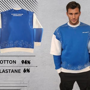 May include: Blue and white sweatshirt with a white collar and white sleeves. The sweatshirt has a white print on the front that says "NO ONE BUT OURSELVES CAN DEGRADE US". The sweatshirt also has a white print on the back that says "DON'T GIVE UP".
