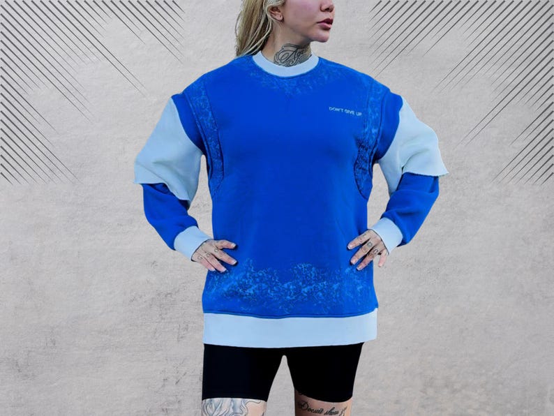 May include: A blue and light blue sweatshirt with a white graphic print. The sweatshirt has a crew neck and long sleeves.