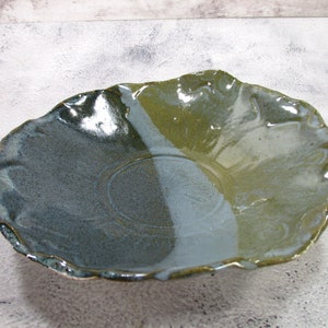 May include: A large, ceramic serving bowl with an irregular, wavy rim. The bowl is glazed in shades of blue, green, and white, creating a mottled effect.