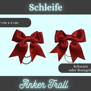 Könnte beinhalten: Zwei bordeauxfarbene Haarschleifen aus Satin, jeweils 7 cm x 5 cm groß, mit einem schwarzen Gummiband. Die Schleifen werden vor einem hellblauen Hintergrund präsentiert. Der Text auf dem Bild lautet "Schleife" und "Anker Troll".
