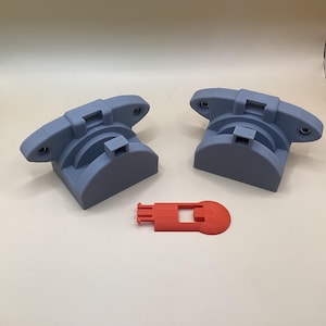 May include: Two grey, 3D-printed, semi-circular objects with a rectangular slot and two holes, and a small red rectangular piece with a circular end. The objects are on a white surface.