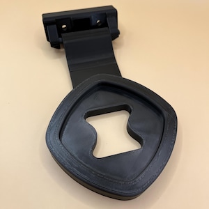May include: A black plastic 3D printed phone holder with a curved base and a hook on the top. The hook is designed to hang over a door or other object.