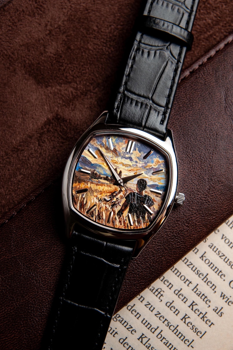 May include: A wristwatch with a silver-toned cushion-shaped case and a black embossed leather strap. The watch face features a detailed impressionistic painting of a person standing in a golden wheat field under a cloudy sky, with silver markers.
