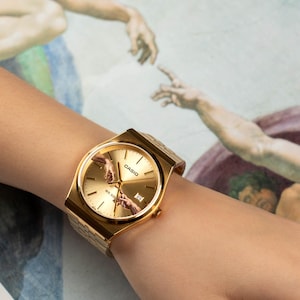 May include: Gold-toned Casio watch with a rectangular face and a gold band. The watch face features the iconic 'Creation of Adam' artwork. The watch is displayed on a wrist against a backdrop of the same artwork.