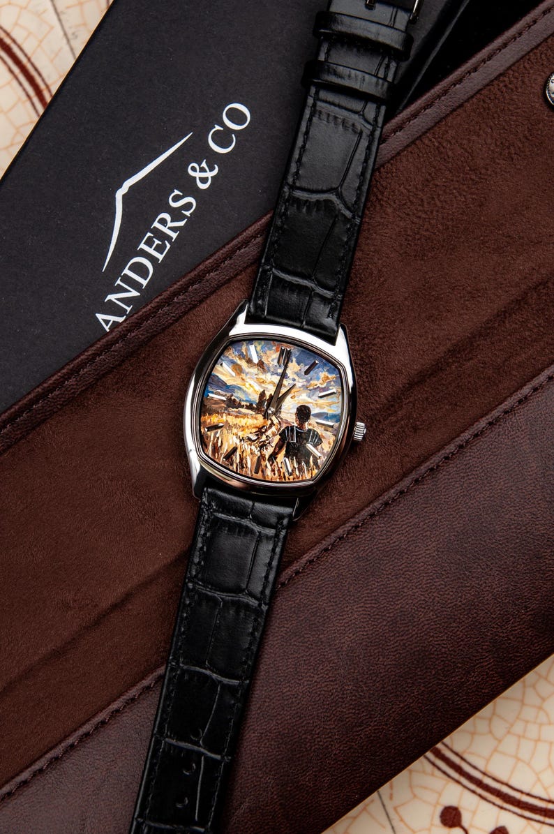 May include: A wristwatch with a black crocodile-embossed leather strap and a silver-tone case. The watch face features a detailed painted scene of a person standing in a golden wheat field under a sunset sky. The brand name ANDERS & CO is visible.