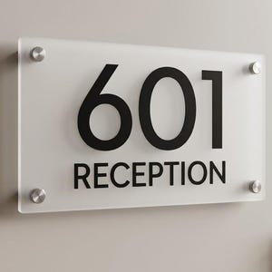 May include: A rectangular frosted acrylic sign featuring the black text 601 and RECEPTION. The sign is mounted with four circular silver-toned metal standoffs at each corner, securing the translucent panel to the wall surface.