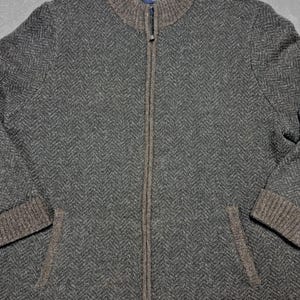 May include: A gray zip-up sweater with a herringbone pattern. The sweater has a high collar, two front pockets, and a zipper closure. The cuffs and collar are a darker shade of gray. The brand name "Pendleton" is visible on the collar.