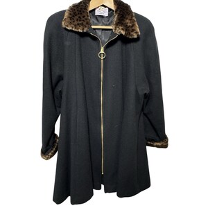 May include: A black coat with a faux leopard fur collar and cuffs. The coat has a gold zipper closure and a flared silhouette. The coat is hanging on a wooden hanger.