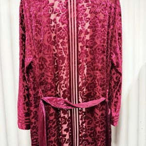 May include: A long, burgundy velvet robe with a floral pattern and a matching belt. The robe has long sleeves and a vertical striped design down the center. The fabric appears soft and luxurious.