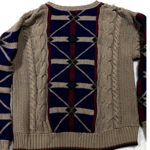 May include: A long-sleeved knit sweater featuring a central panel with a dark blue and maroon geometric diamond pattern. The sweater includes vertical cable knit sections in tan, flanking the central design, with matching tan ribbed cuffs and hem.