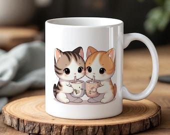 Può includere: Tazza in ceramica bianca con un'immagine di cartone animato di due gatti che bevono da tazze. I gatti sono marroni e bianchi e arancioni e bianchi. La tazza ha un manico nero.