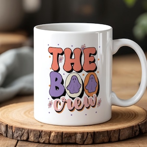 May include: White ceramic mug with the text "The Boo Crew" in orange, purple, and pink. The design includes ghost illustrations and floral accents, perfect for Halloween.