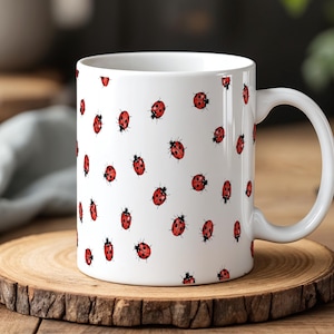Peut inclure: Mug en céramique blanche orné d'illustrations de coccinelles rouges. La tasse a une anse incurvée et repose sur un dessous de verre en bois. Les coccinelles sont dispersées sur la surface de la tasse.