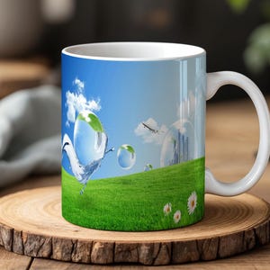 May include: White ceramic mug featuring a vibrant landscape design. The design includes a blue sky with clouds, a green grassy hill, and water droplets with leaves. The mug has a white handle and is set on a wooden coaster.