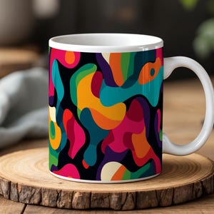 May include: White ceramic mug with a colorful abstract design featuring a black background and various shades of blue, green, yellow, orange, pink, and purple.