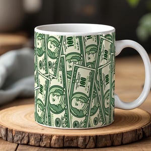 Peut inclure: Mug en céramique blanche avec un motif répété de billets de 100 $ verts et crème. La tasse a une anse blanche et est posée sur un dessous de verre en bois. Le motif recouvre toute la surface de la tasse.