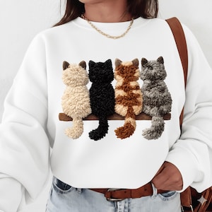 Könnte beinhalten: Weißes Sweatshirt mit einem Design von vier Katzen, die auf einem Holzast sitzen. Die Katzen sind in den Farben Creme, Schwarz, Braun und Grau gehalten. Das Sweatshirt hat einen Rundhalsausschnitt und lange Ärmel.