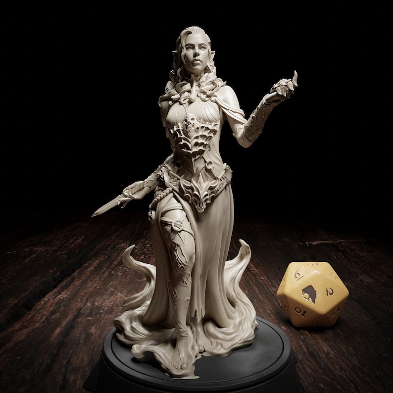 May include: An off-white fantasy figurine of a woman in a flowing gown, holding a dagger and a small object. The figure stands on a black base, with a large, yellow, multi-sided die nearby. The figurine's design includes intricate armor and flowing fabric.