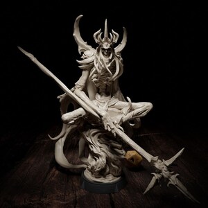 May include: An off-white fantasy figurine depicting a skeletal figure with a horned crown, seated and holding a spear. The figurine sits on a black base, with a wooden surface in the background. A yellow die is near the spear.