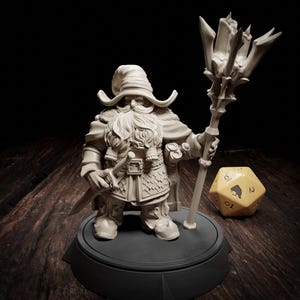 May include: A detailed, off-white figurine of a dwarf wizard, holding a staff with a crystal-like top and a sword. The dwarf has a long beard, hat, and detailed clothing. A large, yellow, twenty-sided die is next to the figure.