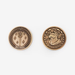 May include: Two circular bronze-toned metal coins. The left coin features a spatula icon surrounded by a laurel wreath and the text READY. The right coin depicts a dog wearing a laurel wreath, surrounded by small fish icons and the text EXHAUSTED.