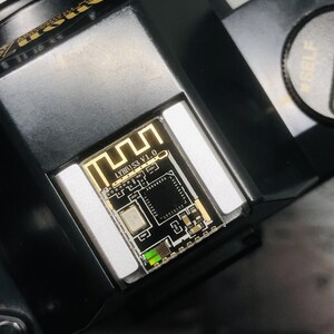 May include: Close-up of a black electronic component with a gold-colored circuit board. The board has the text "LYBB!S3 V1.0" and a Wi-Fi symbol. The component is set in a black housing.