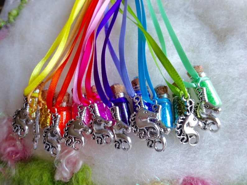 May include: A selection of miniature glass bottles filled with coloured glitter, each sealed with a cork. They hang from satin ribbons in rainbow hues. Silver unicorn charms are attached to the ribbons.