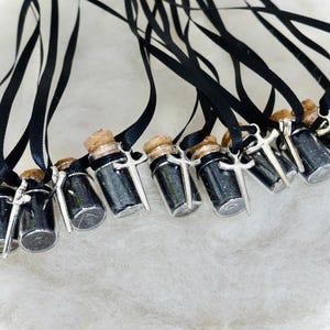 May include: A group of small glass vials with black glitter and a silver sword charm attached to a black ribbon. The vials are hanging from the ribbon.