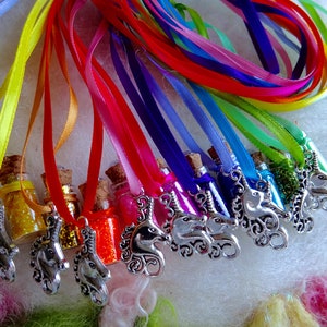 May include: A selection of miniature glass bottles filled with glitter in various colours, each sealed with a cork. The bottles are suspended from colourful ribbons and feature a silver unicorn charm. The ribbons are arranged in a rainbow spectrum.
