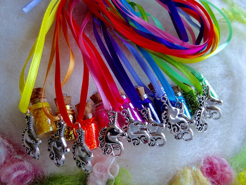 May include: A selection of miniature glass bottles filled with glitter in various colours, each sealed with a cork. The bottles are suspended from colourful ribbons and feature a silver unicorn charm. The ribbons are arranged in a rainbow spectrum.