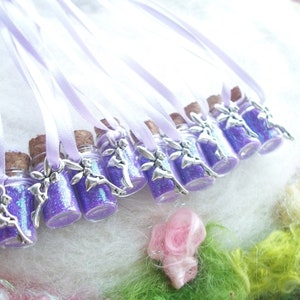 May include: A collection of small glass bottles filled with purple glitter, each with a cork stopper and a silver fairy charm. The bottles are strung on lavender ribbons. The background features a soft, textured surface with pastel-colored accents.