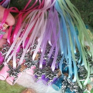 May include: A collection of small glass bottles filled with colorful glitter and topped with a cork and a silver fairy charm. Each bottle is attached to a satin ribbon in a matching color, creating a whimsical and enchanting aesthetic.