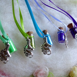 May include: Small glass bottle necklaces filled with coloured glitter, each with a cork stopper and a silver unicorn charm. The necklaces have ribbons in shades of green, blue, and purple.
