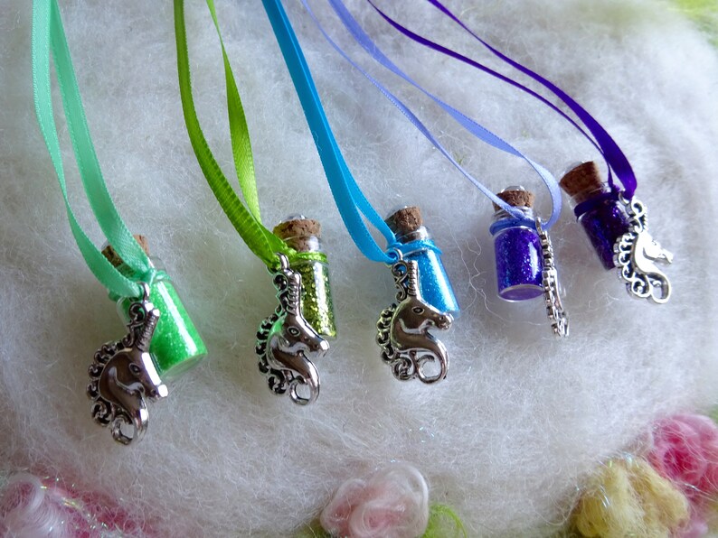 May include: Small glass bottle necklaces filled with coloured glitter, each with a cork stopper and a silver unicorn charm. The necklaces have ribbons in shades of green, blue, and purple.