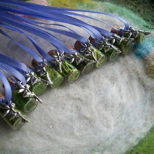 May include: A collection of small glass bottles filled with green moss and topped with silver charms. Each bottle is attached to a blue ribbon, creating a set of necklaces.