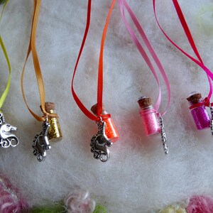 May include: A selection of miniature glass bottles filled with coloured glitter, each suspended by a ribbon. The bottles are decorated with silver unicorn charms. Ribbons are yellow, orange, red, pink, and fuchsia.
