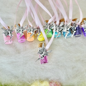 May include: A set of ten small glass bottles with cork tops and silver fairy charms. Each bottle is filled with colorful glitter and attached to a pink ribbon.